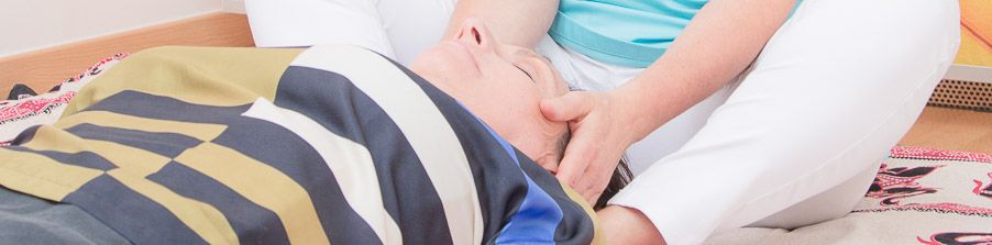 Shiatsu-Behandlung: die Therapeutin hält den Kopf einer liegenden, zugedeckten Patientin